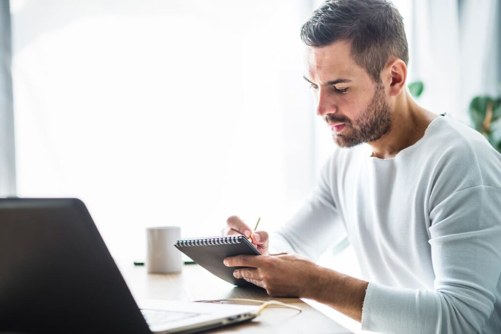 Homme concentré prenant des notes devant son ordinateur pour organiser ses obligations de conformité